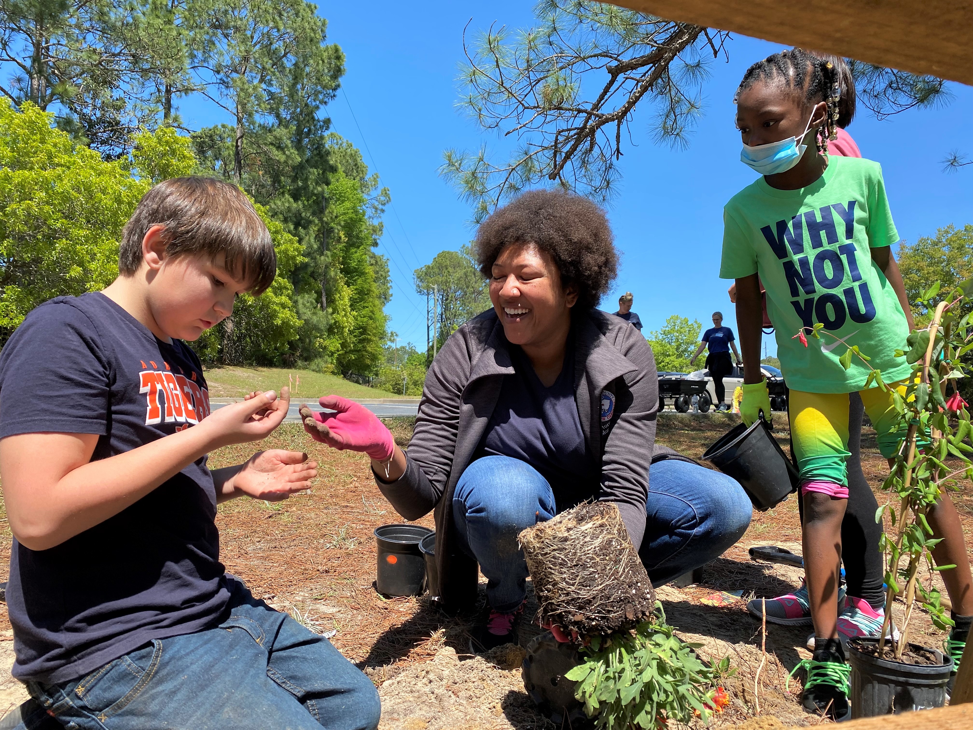 Two students work with an adult to plant a blanketflower in a Carolina Fence Garden