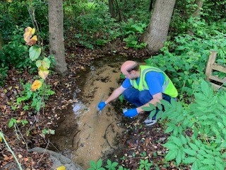 Employee taking a water quality sample in a stream
